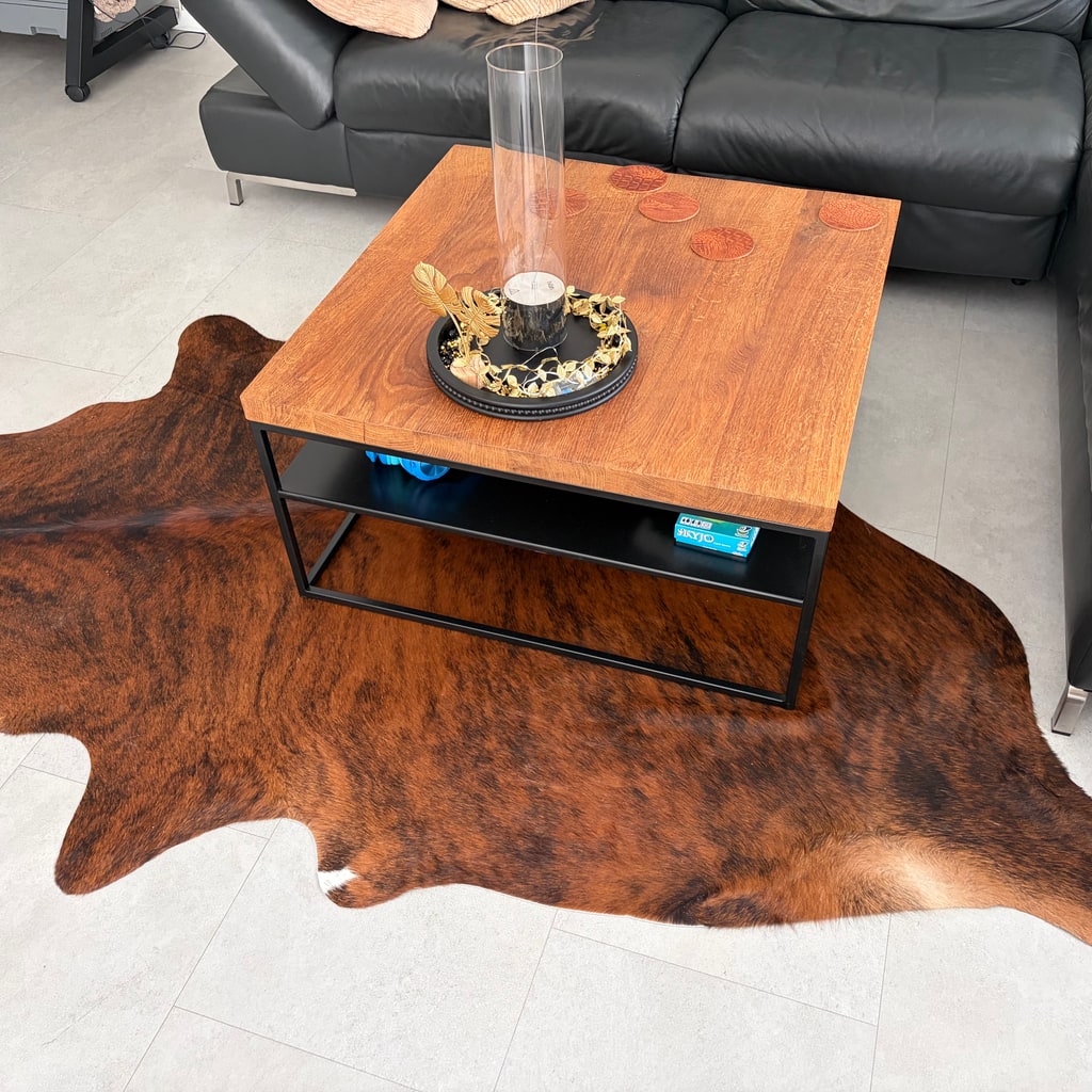 Braun meliertes Kuhfell unter einem Couchtisch in einem Wohnzimmer mit schwarzem Ledersofa.