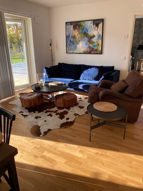 Braun-weißes Kuhfell unter einem runden schwarzen Couchtisch und Lederpoufs neben einem blauen Sofa auf Holzboden.