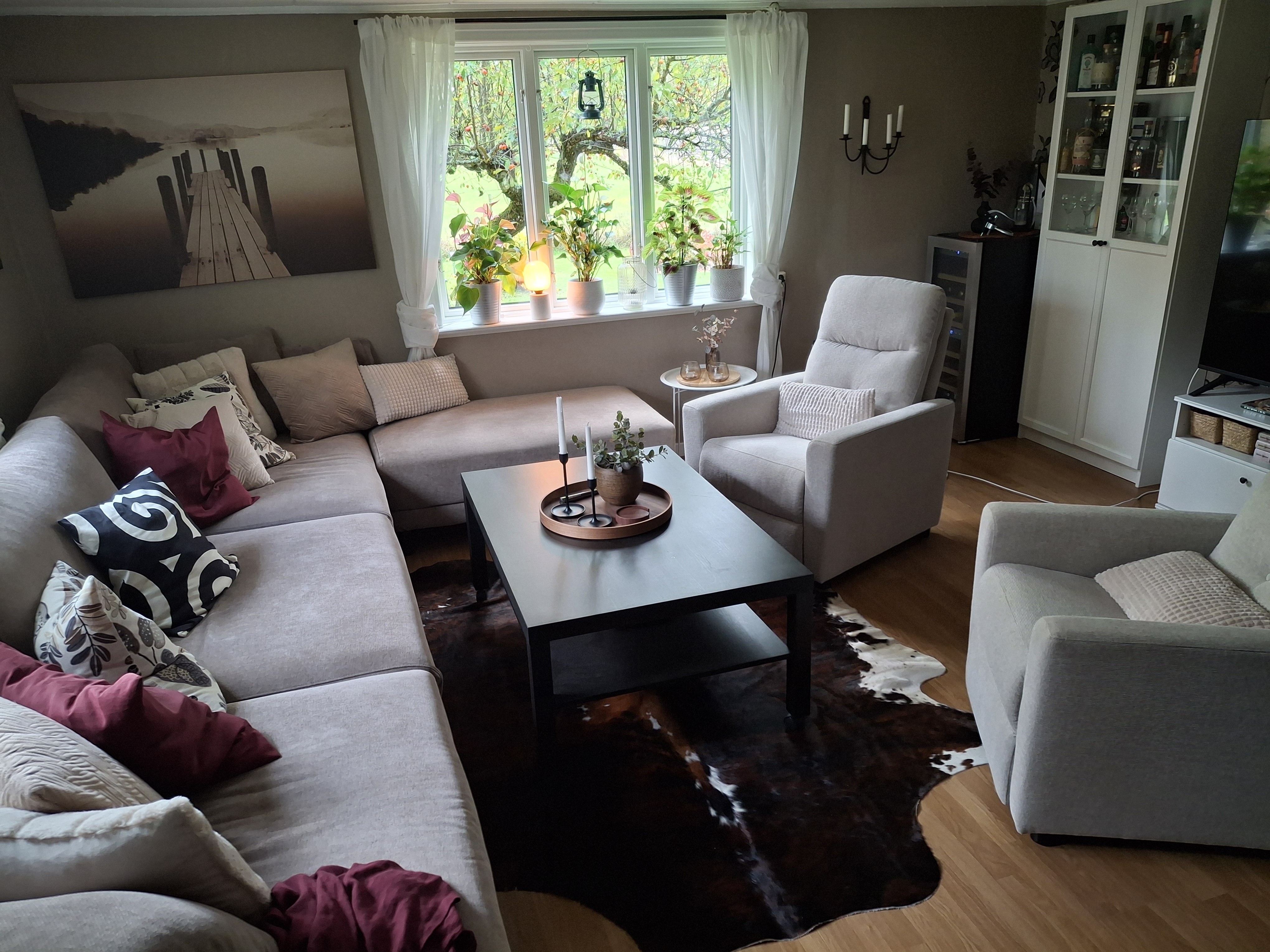 Braun-weißes Kuhfell unter einem dunklen Couchtisch zwischen einem hellen Ecksofa und Sesseln