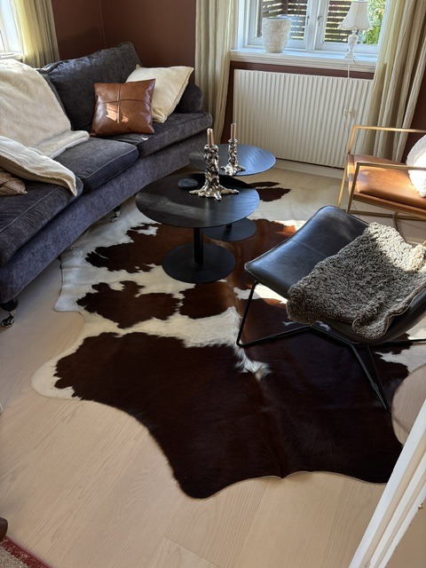 Braun-weißes Kuhfell zwischen einem dunklen Sofa und Sesseln rund um zwei schwarze Couchtische.