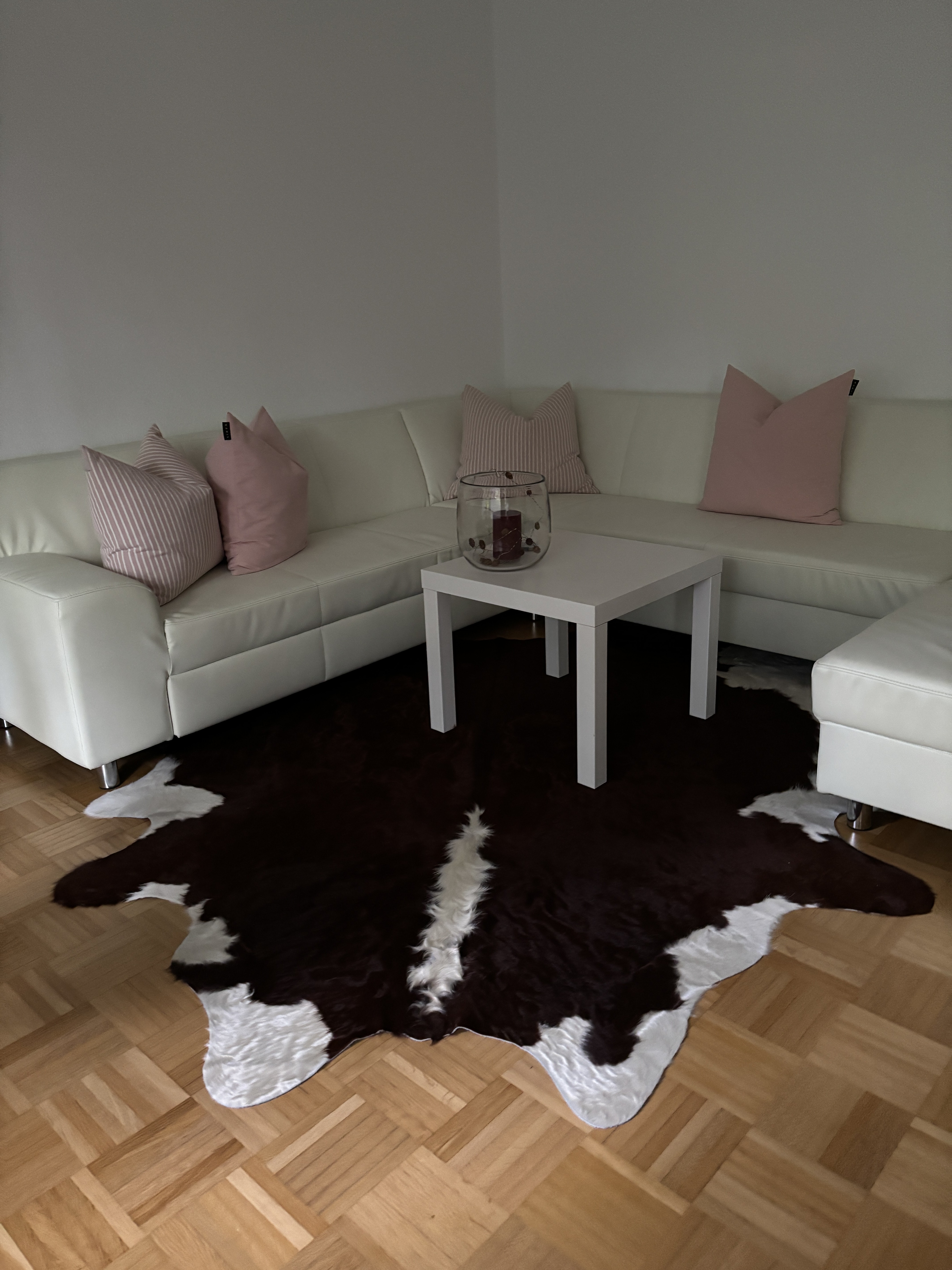 Braun-weißes Kuhfell auf Parkett vor einem weißen Ecksofa mit rosa Kissen