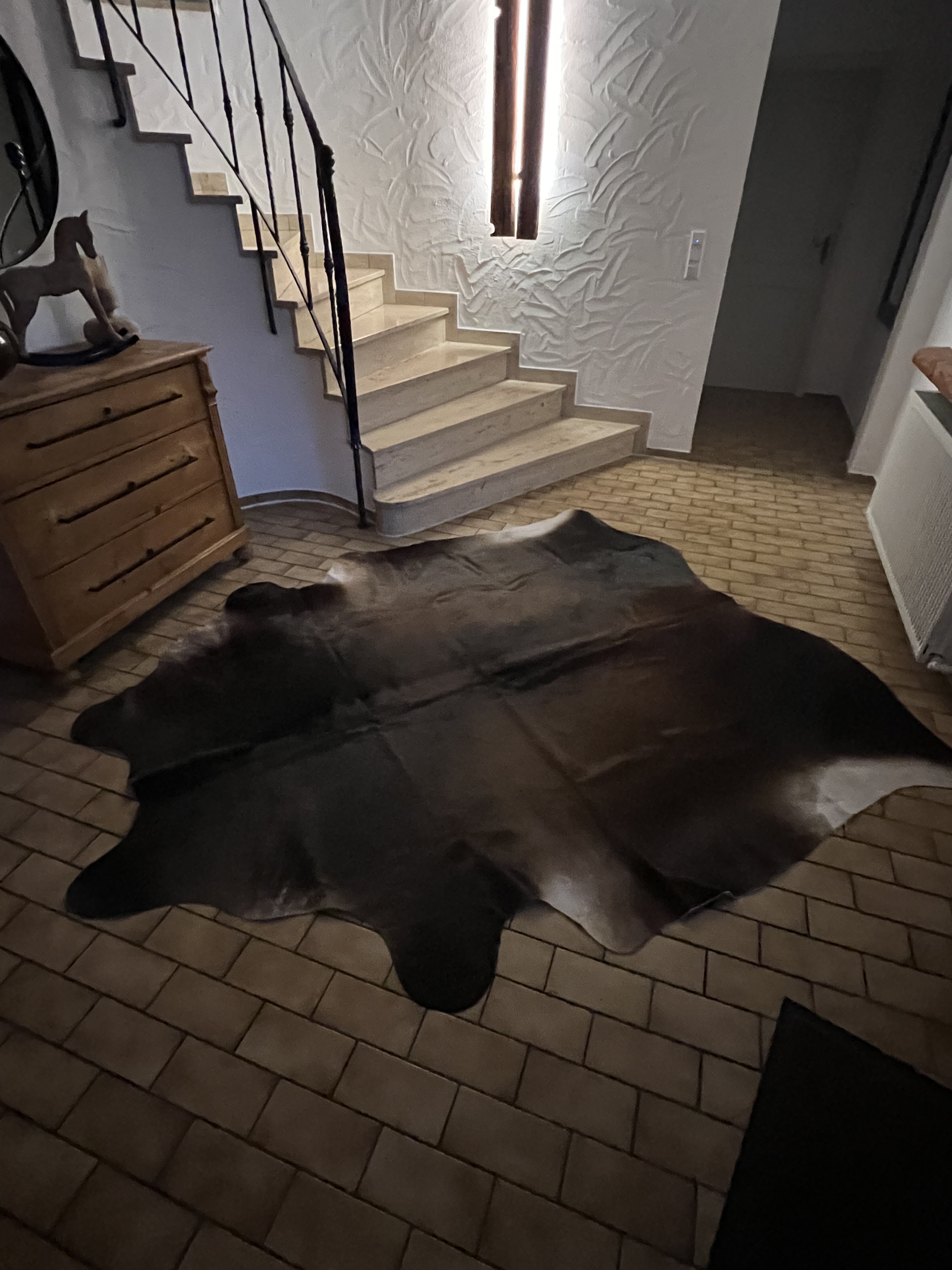Dunkles Kuhfell auf einem Steinboden neben einer hellen Steintreppe und einer Holzkommode